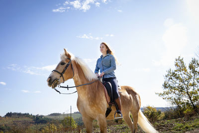 Woman horseback riding in front of sky on sunny day