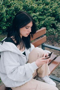 Beautiful teenager girl using smartphone while sitting alone on the bench outdoor on the street.