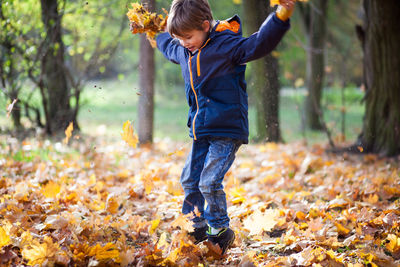 Full length of boy jumping on fallen autumn leaves at park