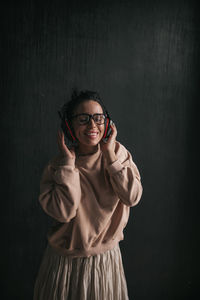 Portrait of smiling young woman standing against black background