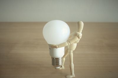 Close-up of figurine carrying light bulb on table against wall