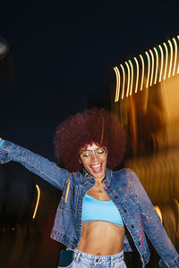 Cheerful female dancing with sunglasses while standing with light effect in evening time