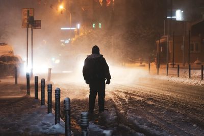 Rear view of man walking on street during winter at night