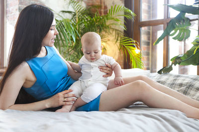 Midsection of mother and daughter sitting on bed