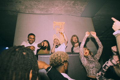 Happy young multiracial men and women dancing around dj at illuminated nightclub