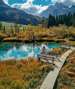 Woman sitting on wooden deck by turquoise lake surrounded by idyllic nature in autumn.