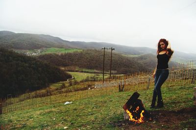Beautiful woman standing by bonfire on mountain during foggy weather