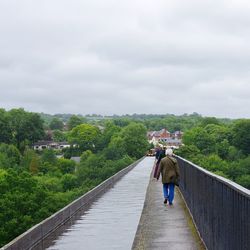 Rear view of people walking on bridge against sky