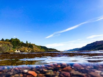 Water surface shot of lake by mountains against blue sky