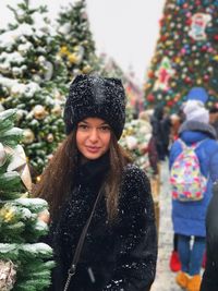 Portrait of young woman standing amidst christmas trees during winter