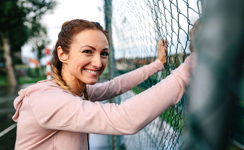 Young sportswoman with boxer braids smiling leaning on a metal fence