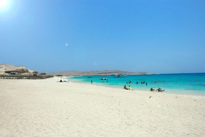 People on beach against clear blue sky