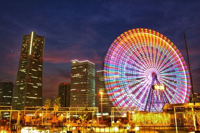 Low angle view of illuminated ferris wheel against buildings at night