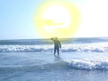 Rear view of silhouette man standing at sea shore against sky