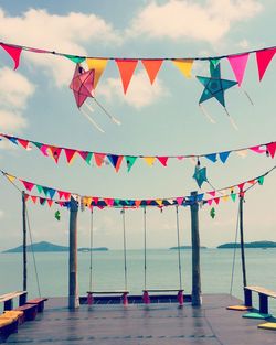 Multi colored flags hanging on sea against sky