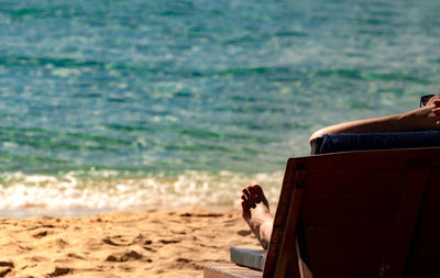Low section of man sitting on lounge chair at beach