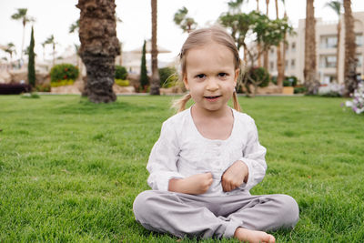 Child sitting on the grass, palm trees on the back. rest in egyptian hotel. portrait