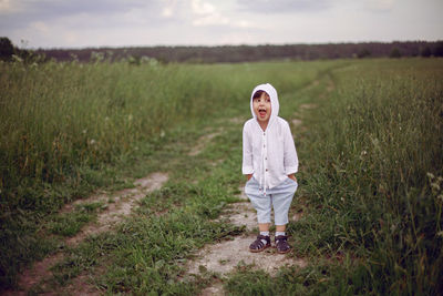 Boy child in a green field in summer in a white shirt with a hood made  linen in shorts and sandals