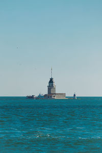 Lighthouse by sea against clear sky