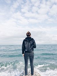 Rear view of woman standing rock by sea against sky