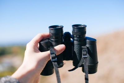 Cropped hand of woman holding binoculars against sky