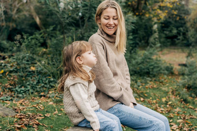 Mom and little daughter play and fool around in the park by the lake.