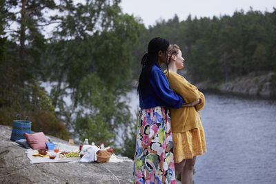 Female couple hugging on cliff by river