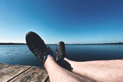 Low section of man sitting on pier by sea against sky