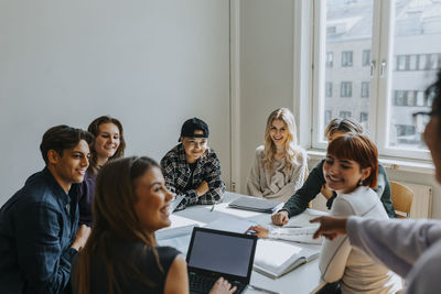 Smiling students looking at teacher pointing in classroom