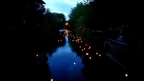 Illuminated city by river against sky