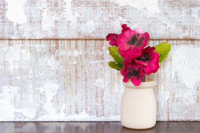 Close-up of rose flower vase on table against wall