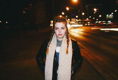 Portrait of young woman standing against light trails on road at night