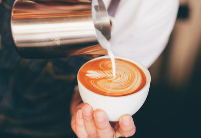 Midsection of barista pouring cream in coffee at cafe