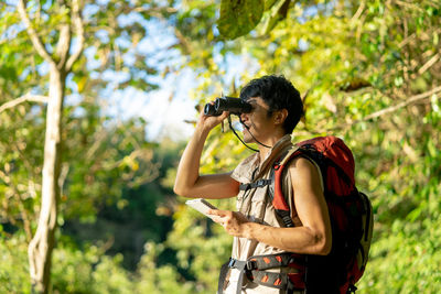 Side view of young woman standing against trees