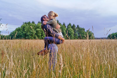 Couple kissing at grassy field against cloudy sky
