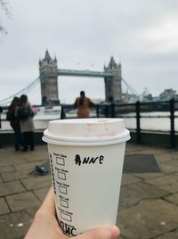 Person holding cup against sky in city