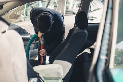 A young man vacuums the interior of a car.