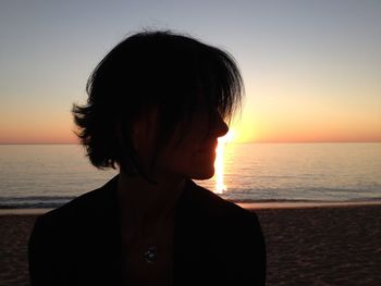 Close-up of woman standing at beach against sky during sunset