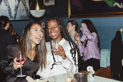 Happy female and male friends having wine during party in bar