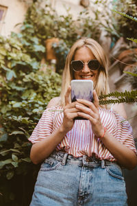 Happy woman with sunglasses looking her smart phone in the nature