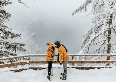 Young couple in matching jackets standing on lookout point over lake. winter, snow, adventure.