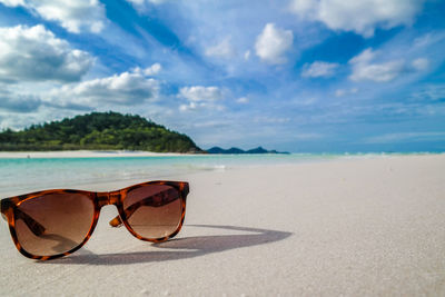 Close-up of brown sunglasses on sand at beach against sky