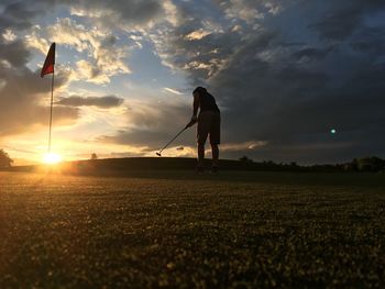 Man playing on golf course against sky during sunset