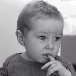 Close-up of cute sad baby boy looking away while biting finger