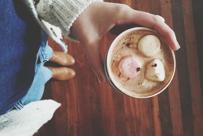 Cropped image of woman holding marshmallow in hot chocolate