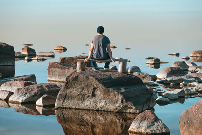 Rear view of man sitting on bench at beach