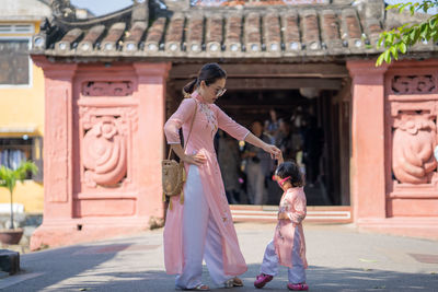 Mother and daughter dancing on footpath by built structure