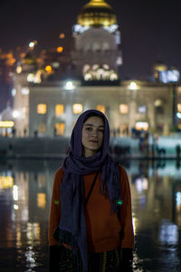 Portrait of woman standing against illuminated temple at night