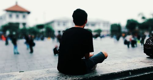 Rear view of man sitting on footpath