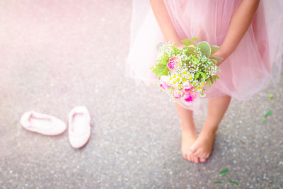 Low section of girl holding flower bouquet while standing on road during wedding